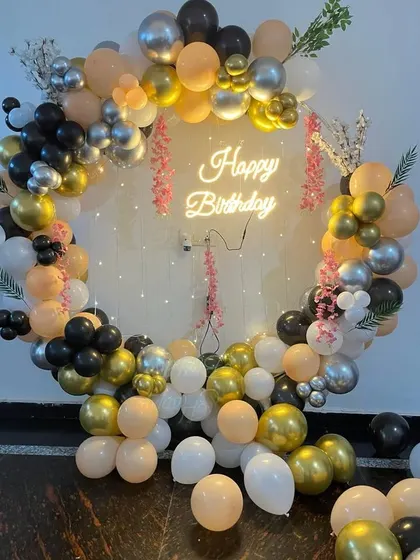 A chic balloon ring with a mix of black, peach, gold, and white balloons. The fairy lights and small floral details add a touch of elegance to this modern design.