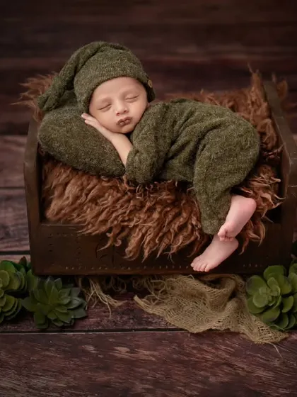 A full view of our little green-clad newborn, sleeping soundly on a rustic wooden bed.