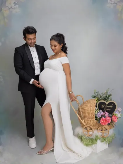 Announcing twins with a beautiful prop. The couple looks down at a lovely wicker pram filled with flowers, a creative and charming way to signify they are expecting two bundles of joy.