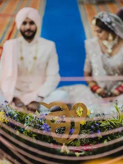 A beautifully framed shot of the couple during their Anand Karaj ceremony, with the 'Ek Onkar' symbol in the foreground, emphasizing the spiritual nature of their union.