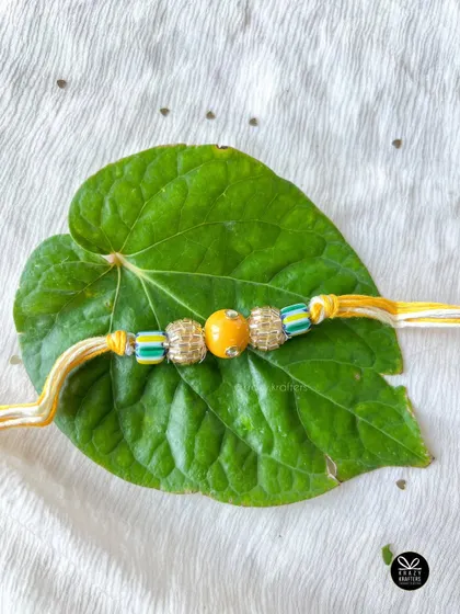 A beautiful, minimalist rakhi with yellow and green beads, resting on a paan leaf for a traditional touch.