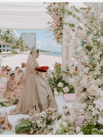 A beautiful wide shot of a beachside Anand Karaj ceremony. The bride is surrounded by flowers and family, with the ocean as a stunning backdrop.