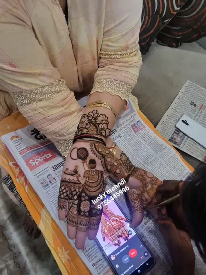A Karwa Chauth design in progress. You can see the classic motif of a woman with a sieve, being drawn carefully on the palm, with a phone used for design reference.