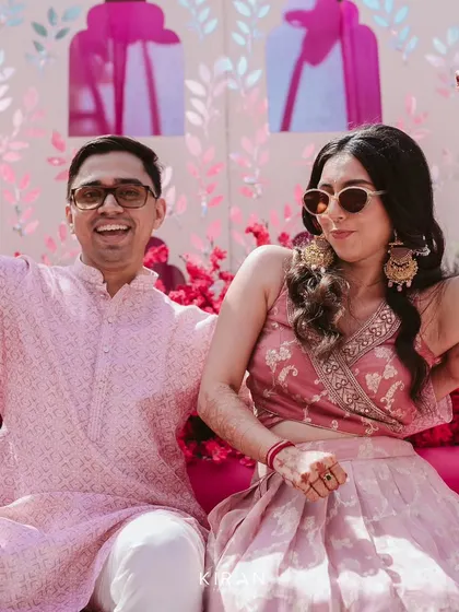A moment of pure celebration at the Mehendi. The couple's energy is matched by the vibrant pink floral decor that surrounds them.