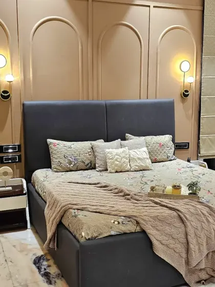A close-up of the bed area, showing the elegant wall moldings, modern sconce lighting, and plush bedding that create a welcoming atmosphere for guests.