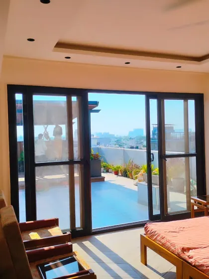 A view from inside the Palam Vihar terrace room, looking out onto the landscaped rooftop on a bright, sunny day.