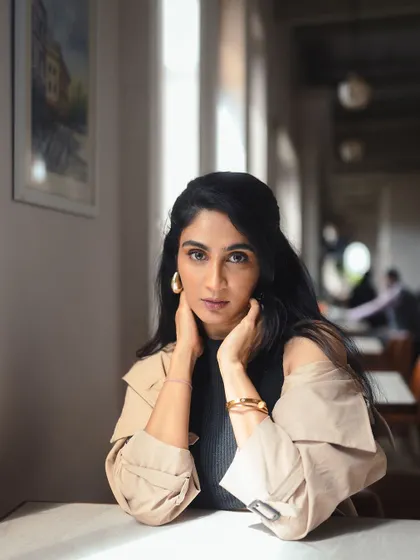 This pose highlights the gold hoop earrings and the clean lines of the trench coat's collar.