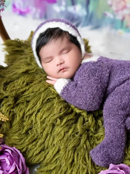 Dreaming in a field of lavender. This newborn is dressed in a cozy purple outfit, surrounded by beautiful floral arrangements for a vibrant and gentle portrait.
