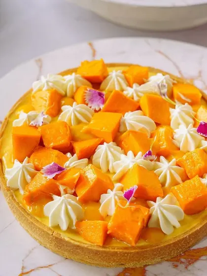 A full mango tart on a marble platter. The elegant styling and lighting make this a sophisticated shot suitable for high-end bakeries and patisseries.