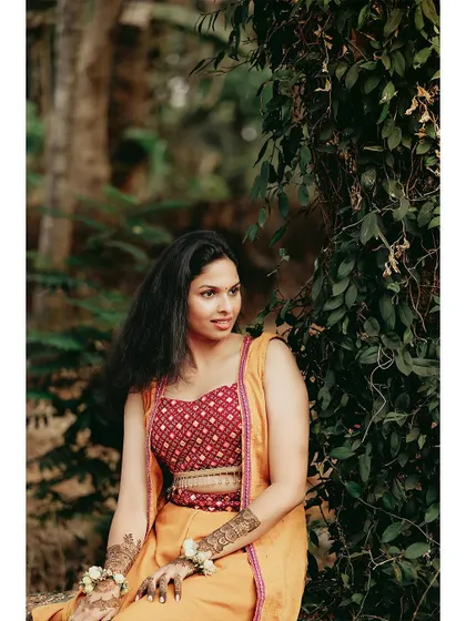 A beautiful portrait of the bride in her Haldi outfit, sitting in a natural, rustic setting.
