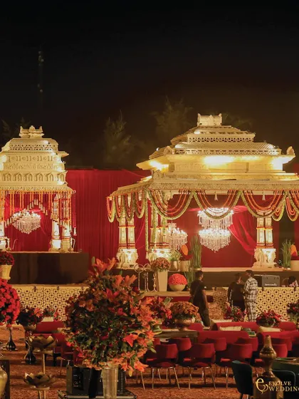 Another perspective of the grand mandap structures, highlighting the intricate craftsmanship of the temple-inspired canopies against the night sky. The warm lighting enhances the architectural details and creates an inviting atmosphere.