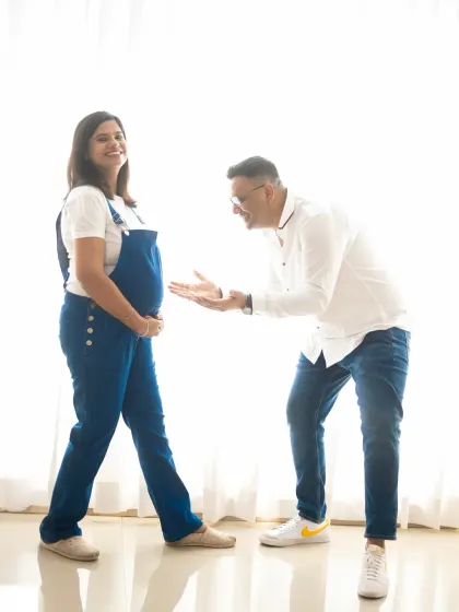 A playful and candid moment during a casual maternity shoot. The dad-to-be's expressive gesture towards the baby bump is full of joy.