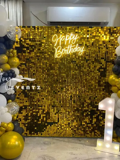 I designed this glamorous and modern birthday backdrop using a gold shimmer wall. The setup is framed by an organic balloon garland in black, white, and gold, and features a 'Happy Birthday' neon sign and a large marquee number '1' to mark the special occasion.