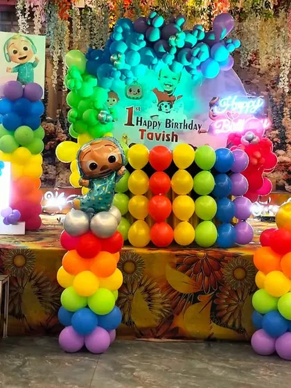 A Cocomelon themed first birthday stage glowing with colorful lights. The neon sign and bright balloons make the setup look even more magical.