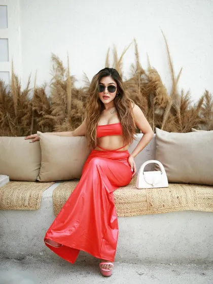 A seated pose from the red dress shoot, showcasing the full outfit against a rustic, bohemian-style bench.