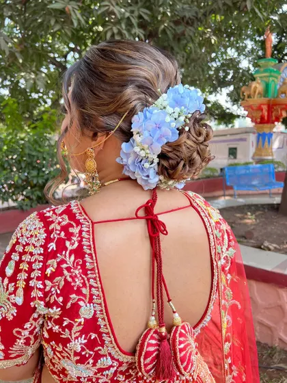 A beautiful shot of the back of the bride's hairstyle, featuring a bun adorned with blue and white flowers to match her red lehenga.