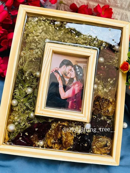 A top-down view of the pinewood frame, showing the preserved engagement bouquet flowers and pearls surrounding the inset photo.