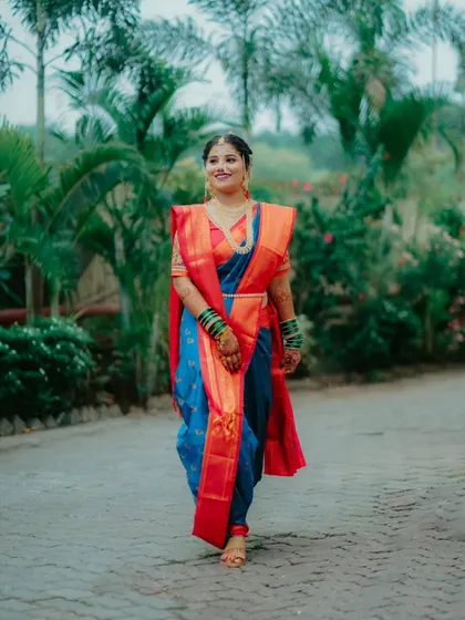 A full length shot of the bride walking gracefully in her vibrant blue and red Navvari saree, a picture of traditional elegance.