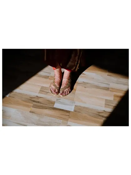 A detail shot of the bride's feet, adorned with henna and beautiful sandals, standing in a sliver of light.