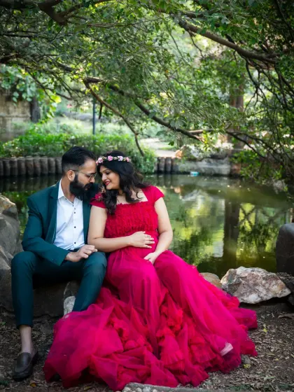 A serene moment for an expecting couple, seated by the water in a quiet park. The rich color of her gown and the natural setting create a beautiful and peaceful maternity portrait.