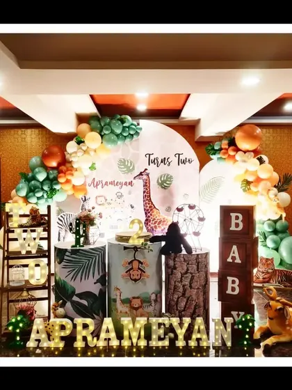 Aprameyan's second birthday was a jungle celebration filled with realistic animal figures and lush greenery. The setup includes marquee letters, themed pedestals, and a balloon arch in jungle-inspired colors, creating a fun and photogenic party space.
