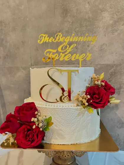 A closer look at the details on this two-tier wedding cake, showing the intricate lace texture on the bottom tier and the elegant placement of the custom initial and "The Beginning of Forever" toppers.