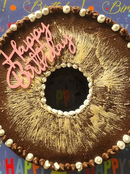 A top down view of my donut shaped chocolate ganache cake. It's a simple yet striking design, perfect for any birthday celebration, with a dusting of cocoa and piped vanilla details.