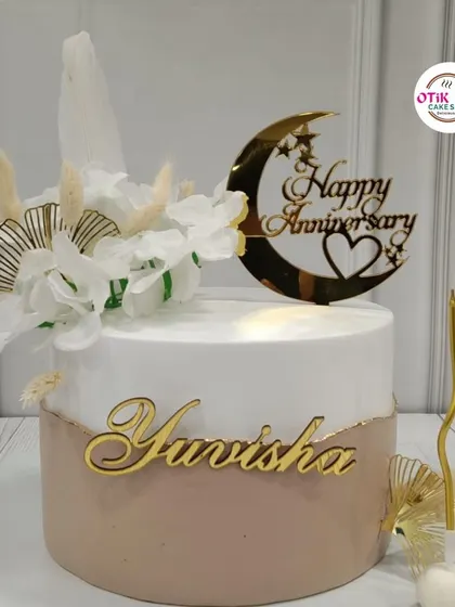 This elegant anniversary cake features a soft beige and white design, accented with dried botanicals and a beautiful gold moon and stars topper.