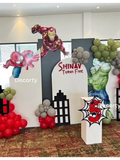A close-up of the superhero backdrop, highlighting the custom 'Shinav Turns Five' sign and character cutouts.