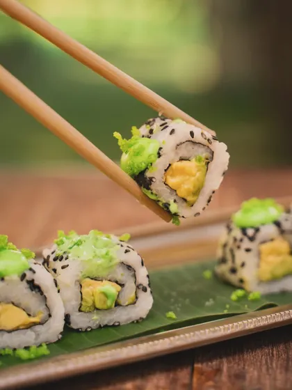 A close-up of sushi being held by chopsticks against a soft, natural background. This shot highlights the fresh ingredients and careful construction of the roll, perfect for an Asian restaurant menu.