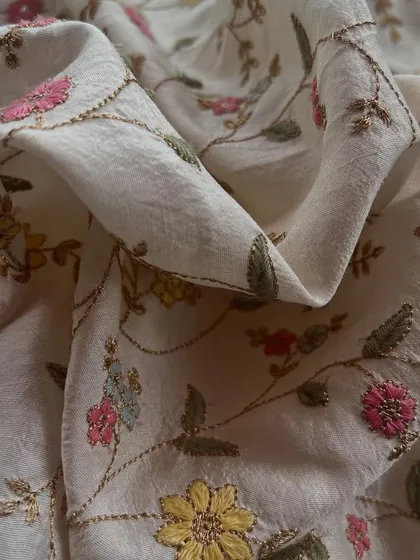 This off-white embroidered slub silk is a vision of elegance. The delicate floral vines are perfect for a graceful saree or a sophisticated Anarkali.