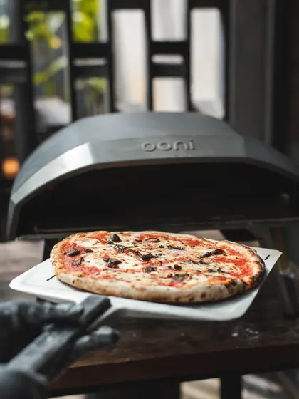 Ready for the fire. A freshly topped pizza on a peel, about to be slid into the portable Ooni oven for a quick, high-heat bake.