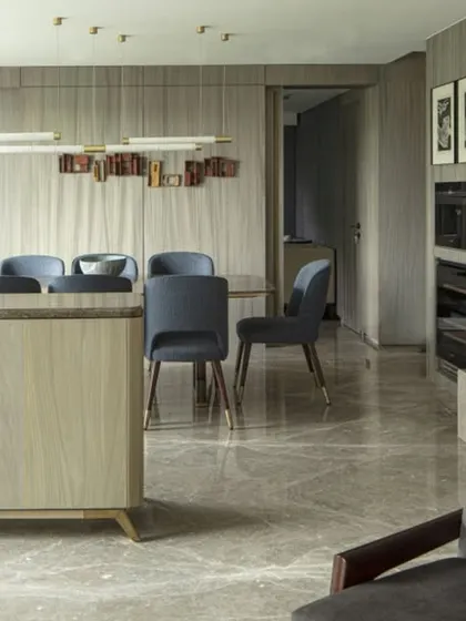 An open-plan living and dining area in the Jor Bagh Residence. The space is defined by its clean lines, luxurious materials like marble flooring and wood-paneled walls, and a carefully selected palette of neutral tones with pops of blue.
