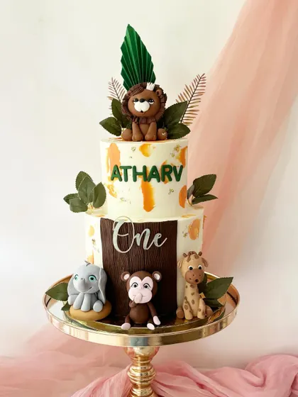 This two-tiered jungle cake for a first birthday has a rustic, wild feel. It includes fondant figures of a lion, monkey, giraffe, and elephant, with a mix of painted and fondant details.