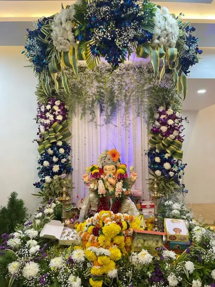 This lush Ganpati decoration uses a mix of blue orchids, white hydrangeas, and fresh greenery. The arrangement creates a rich, textured floral arch that looks both natural and grand.