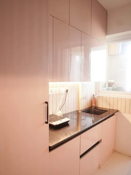 This view of the pink kitchen shows the floor-to-ceiling cabinets, maximizing storage in a compact layout. The natural light from the window enhances the soft, cheerful color of the cabinetry.