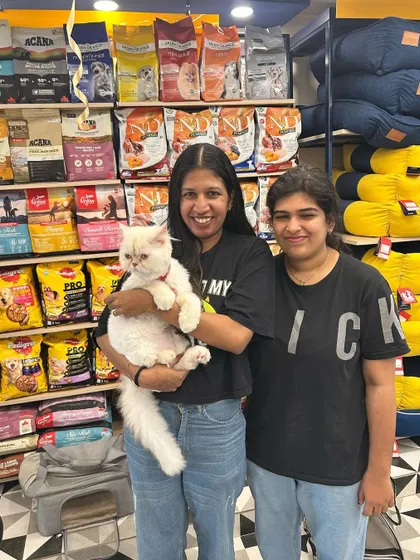 A happy pet parent holding her fluffy white cat at our Meow Fest event, surrounded by shelves of premium cat food.