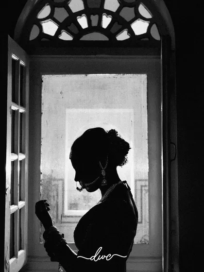 A beautiful black and white silhouette of the bride getting ready by a window, the intricate details of her jewelry still visible.