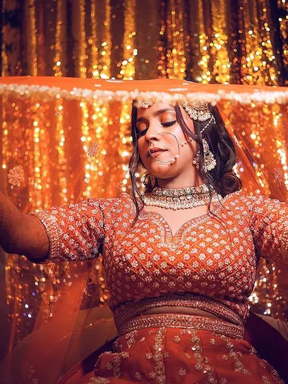The classic shot of the bride holding her veil, captured against a sparkling gold background.