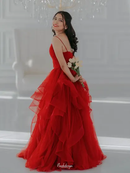 A beautiful solo portrait of the bride-to-be in a vibrant red gown, holding flowers behind her back in a bright, all-white studio.