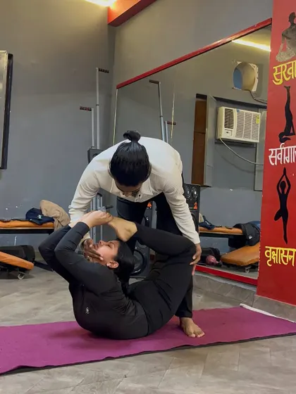 Continuing the adjustment in a deep back-bending pose, helping the student to bring their feet closer to their head.
