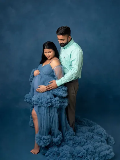 A stunning full-length portrait of an expecting couple. The magnificent blue gown flows around them, creating a dramatic and romantic image against the matching backdrop.