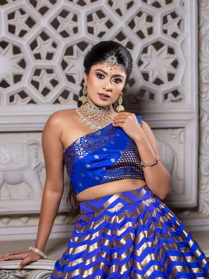 A close-up of the model, highlighting the one-shoulder brocade blouse and statement jewelry.