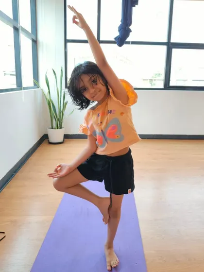 A happy yogini strikes a confident Tree Pose. This classic balancing asana is a favorite in our kids' classes for improving focus and stability.