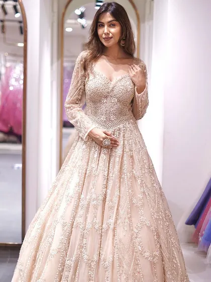 A full-length view of a breathtaking beige gown with long sleeves. The intricate, all-over embellishments create a look of pure luxury and sophistication, perfect for a grand reception.