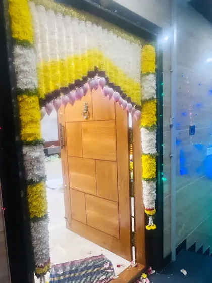 An entrance door decorated with yellow and white flowers, with hanging lotus buds. The lighting from inside gives it a warm glow.