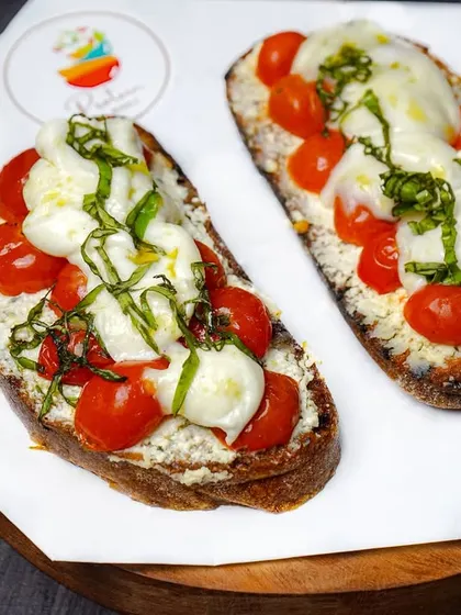 Fresh caprese bruschetta with cherry tomatoes, mozzarella, and basil on a dark wooden board. The contrast between the bright toppings and the dark background is visually striking.