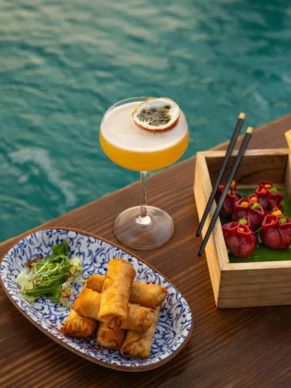 An elegant poolside scene featuring a passionfruit cocktail alongside spring rolls and dumplings, perfect for a resort menu.