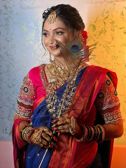 A creative shot of a bride in a blue Paithani, holding a peacock feather that complements her saree's colors.