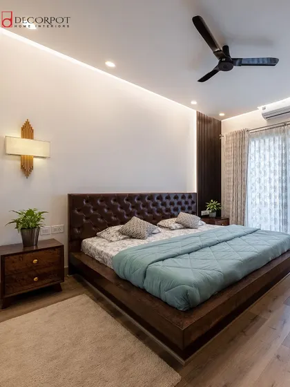 A spacious and luxurious master bedroom with a dark wood bed and a classic tufted leather headboard. The room is filled with natural light, creating a warm and inviting atmosphere.